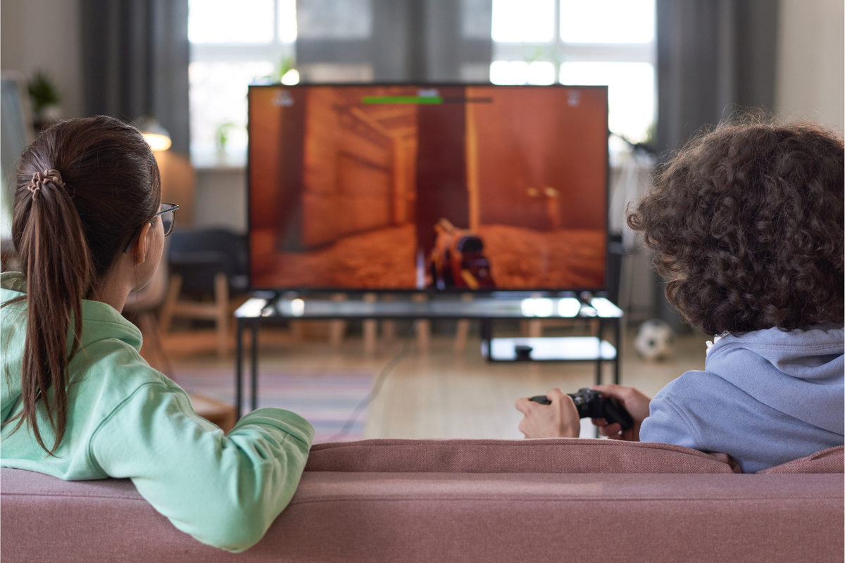 Two teenagers sitting on a couch and playing a console game in a living room